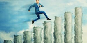 A man in business casual attire leaping confidently across surreal cloud pillars against a vibrant blue sky, symbolizing the wisdom of the crowd and overcoming challenges.