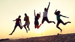 Five friends leap joyfully into the air on a sandy beach, silhouetted against a golden sunset, conveying a sense of freedom and happiness in the moment, their bodies fueled by vitamins for such